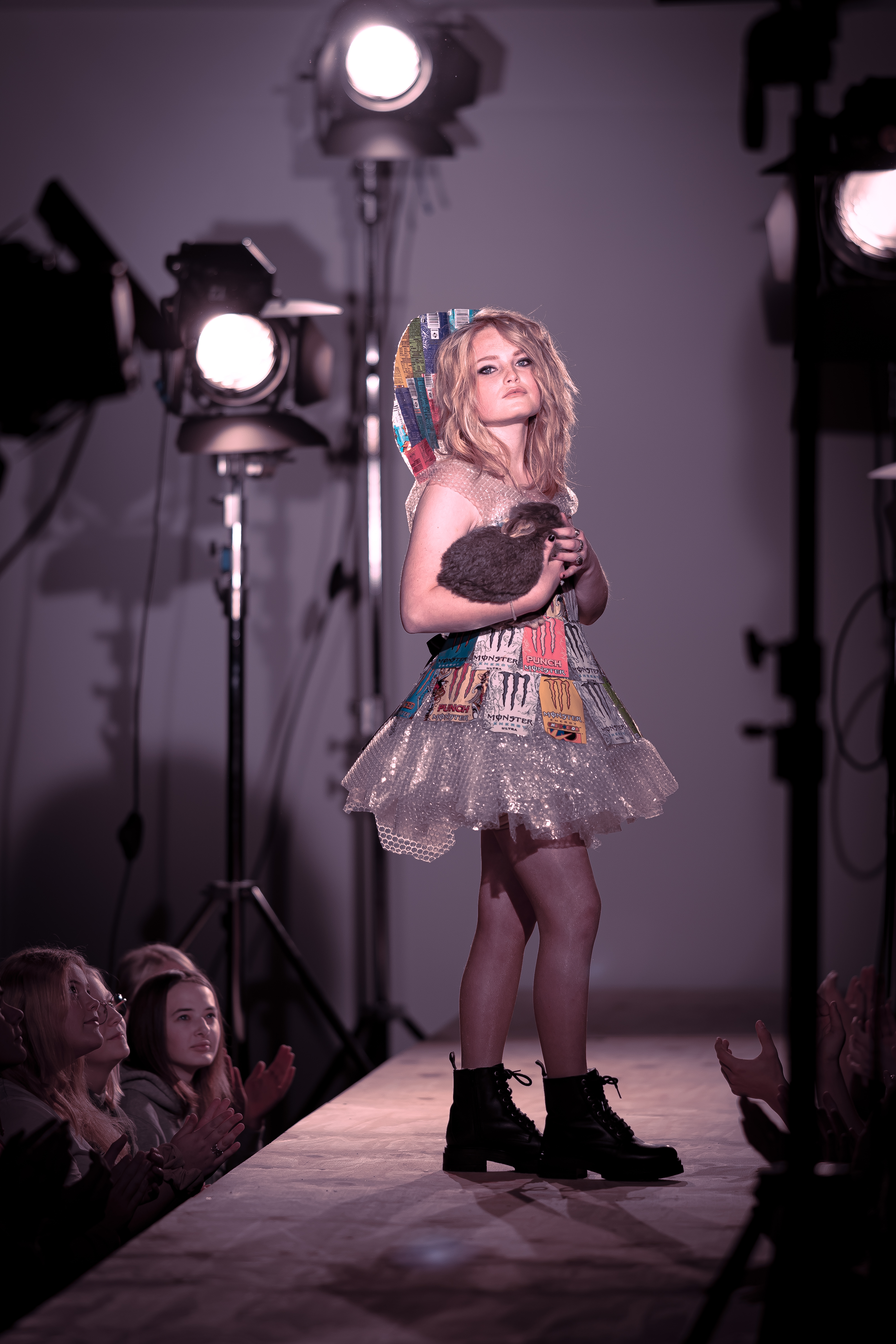 Model præsenterer kreativ kjole på catwalken under modeshow med tilskuere og spotlights