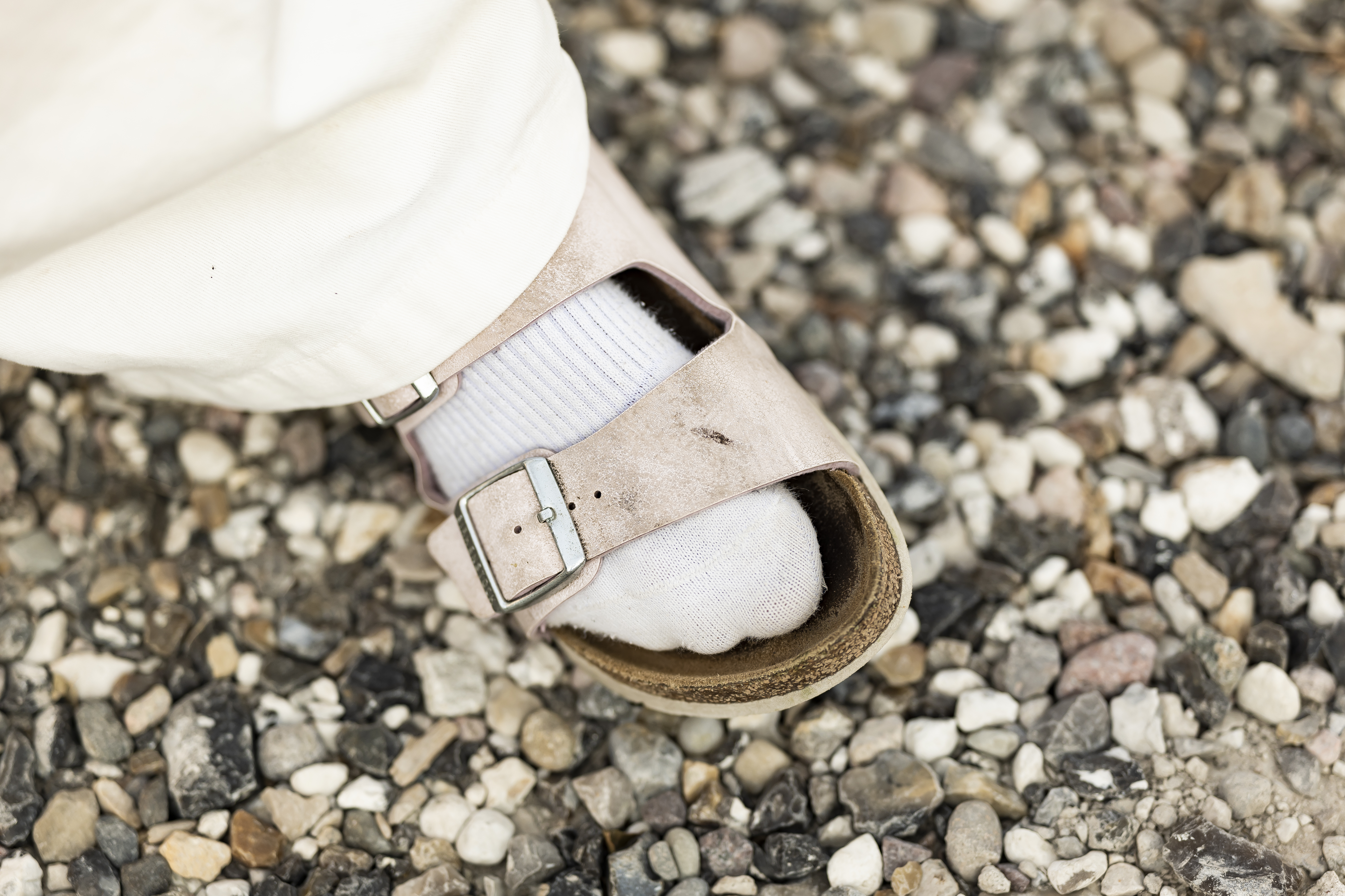 Person i lys kjole og sandaler med spænde går på grusstien