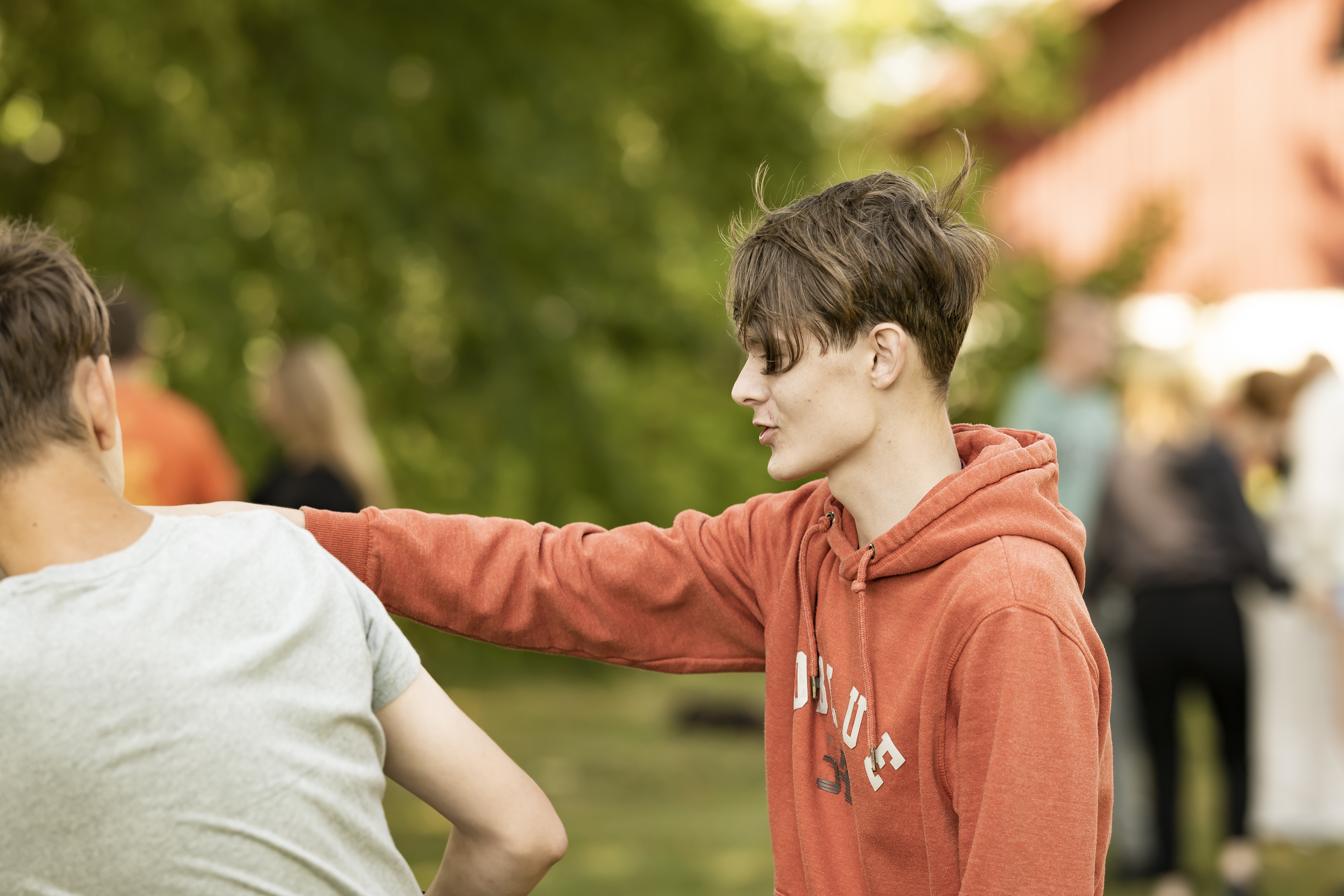 Ung person i orange hættetrøje har armen om skulderen på en anden elev udendørs